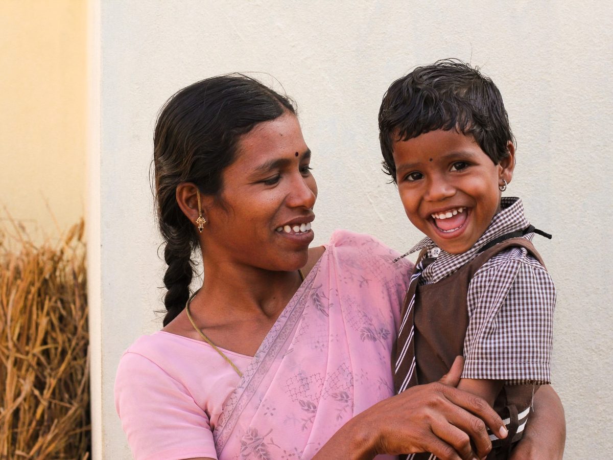 A woman in a pink saree holding a laughing child dressed in a school uniform